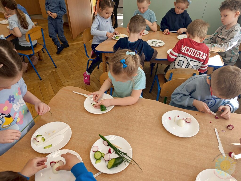 Siedzące dzieci przy stole, które biorą udział w zajęciach gastronomicznych - Przedszkole Samorządowe Nr 2 Pod Słonkiem w Białymstoku