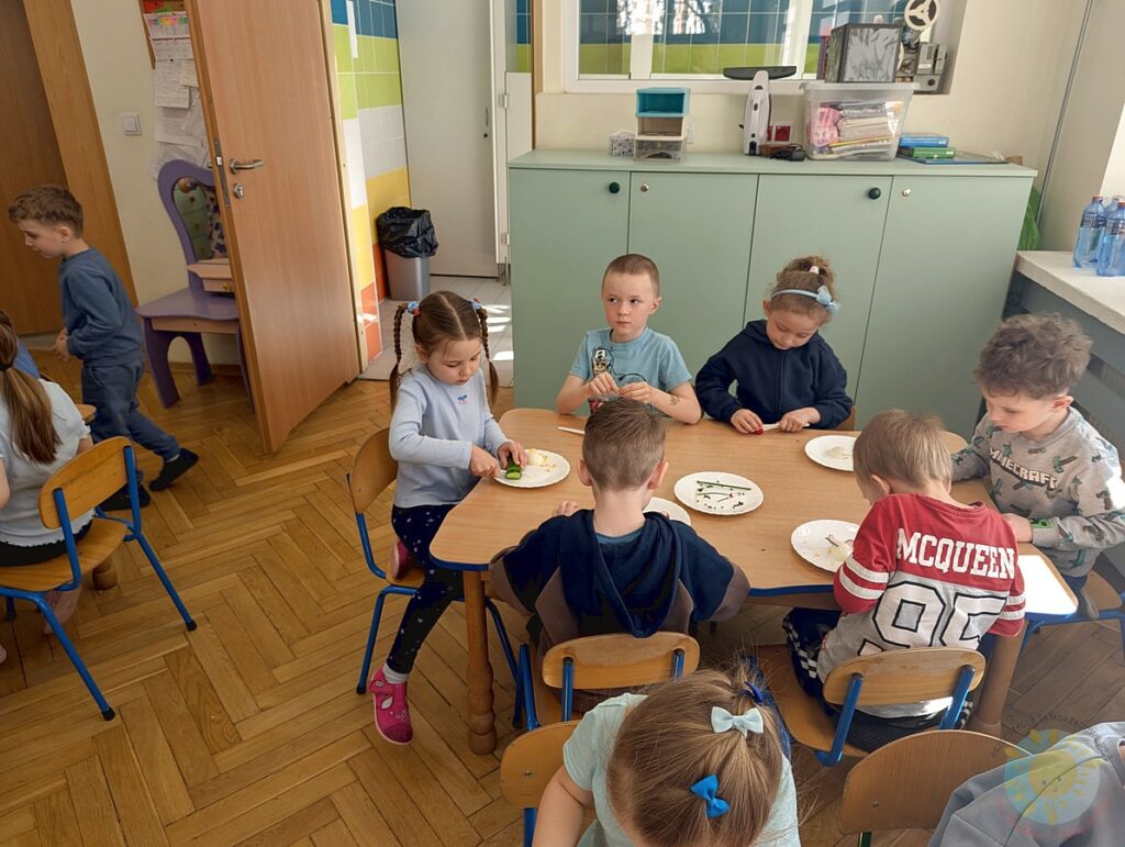 Siedzące dzieci przy stole, które biorą udział w zajęciach gastronomicznych - Przedszkole Samorządowe Nr 2 Pod Słonkiem w Białymstoku