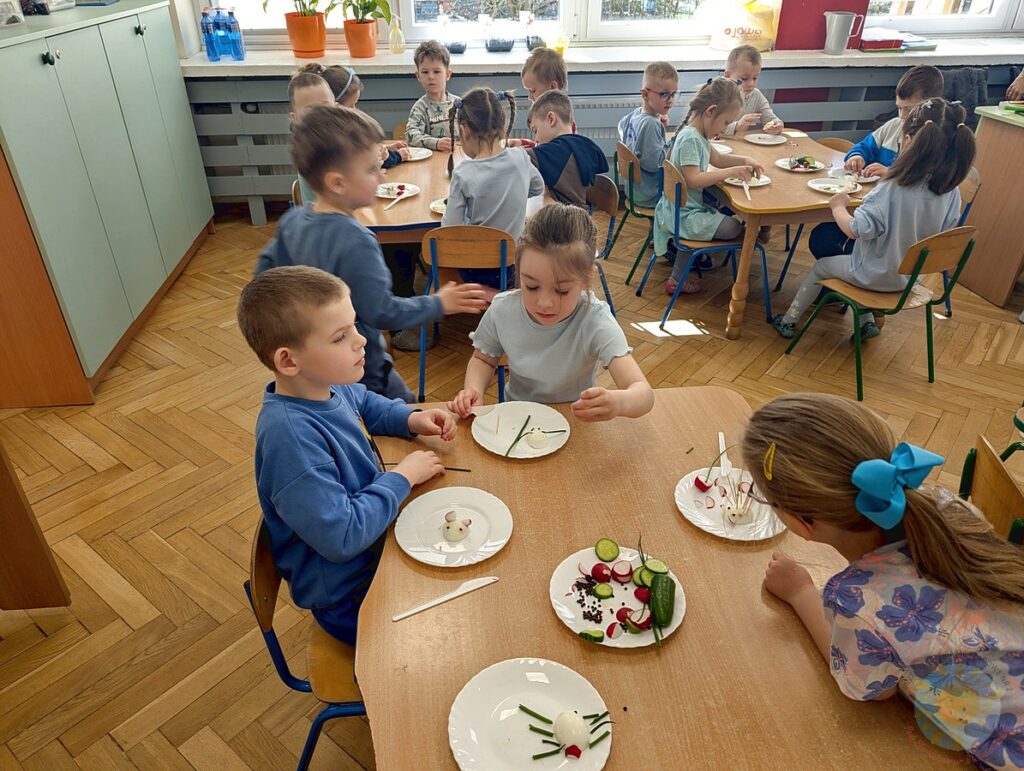 Siedzące dzieci przy stole, które biorą udział w zajęciach gastronomicznych - Przedszkole Samorządowe Nr 2 Pod Słonkiem w Białymstoku