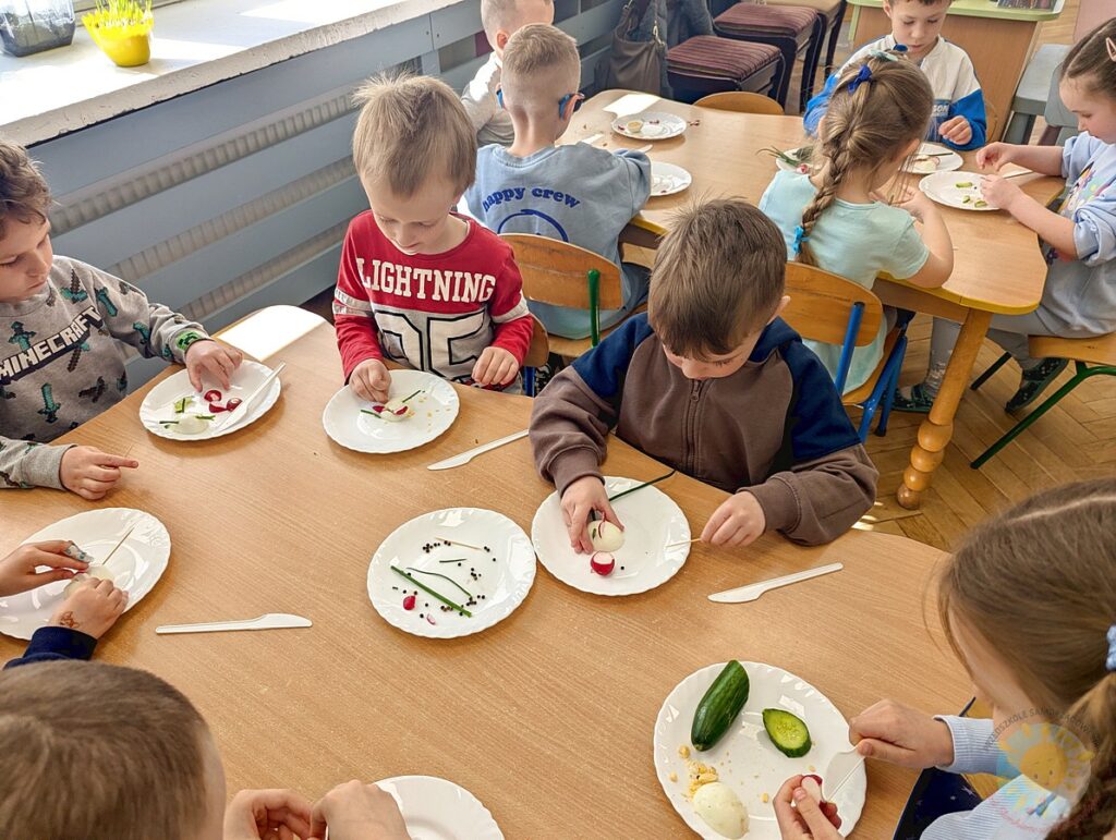 Siedzące dzieci przy stole, które biorą udział w zajęciach gastronomicznych - Przedszkole Samorządowe Nr 2 Pod Słonkiem w Białymstoku