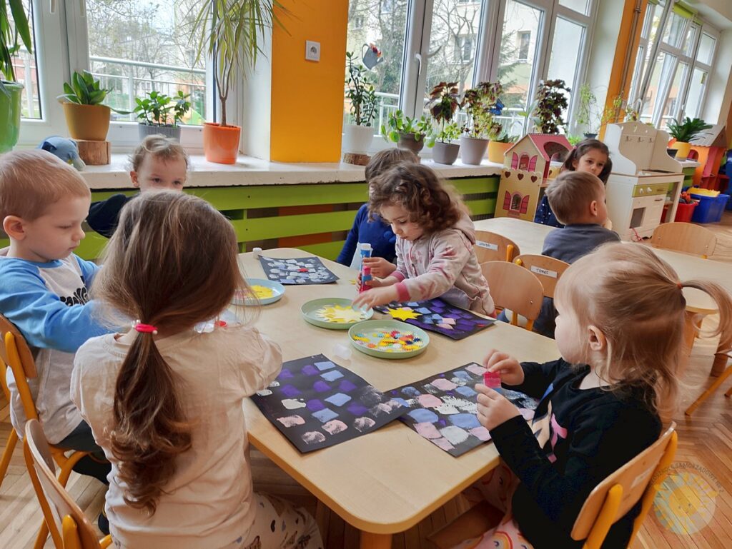 Siedzące dzieci przy stole i wykonują pracę plastyczną - Przedszkole Samorządowe Nr 2 Pod Słonkiem w Białymstoku