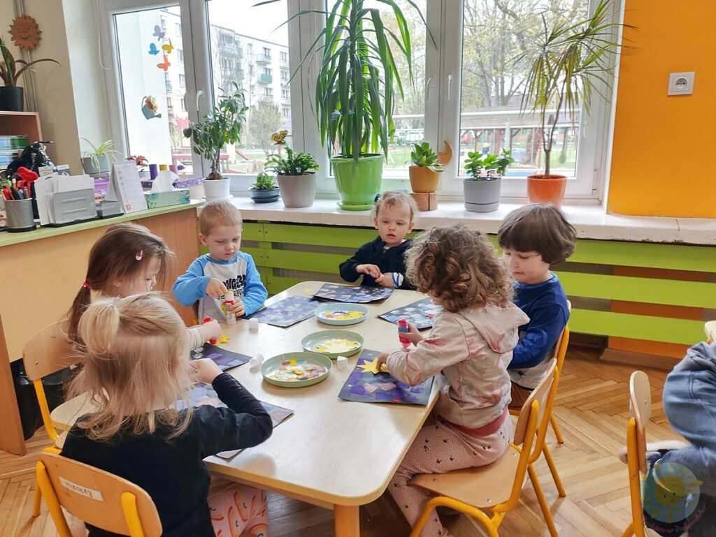 Siedzące dzieci przy stole i wykonują pracę plastyczną - Przedszkole Samorządowe Nr 2 Pod Słonkiem w Białymstoku