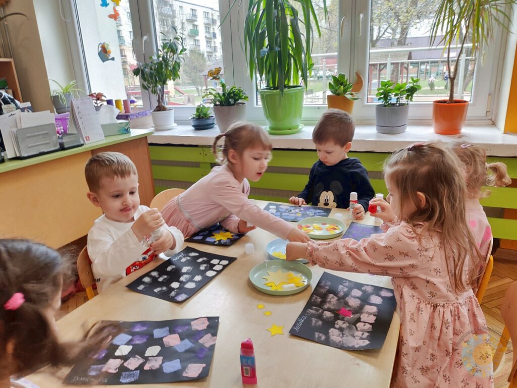Siedzące dzieci przy stole i wykonują pracę plastyczną - Przedszkole Samorządowe Nr 2 Pod Słonkiem w Białymstoku