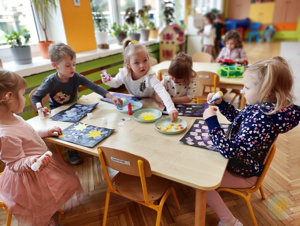 Siedzące dzieci przy stole i wykonują pracę plastyczną - Przedszkole Samorządowe Nr 2 Pod Słonkiem w Białymstoku