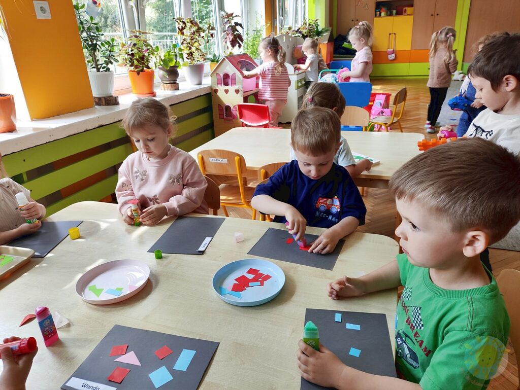 Siedzące dzieci przy stole i wykonują pracę plastyczną - Przedszkole Samorządowe Nr 2 Pod Słonkiem w Białymstoku