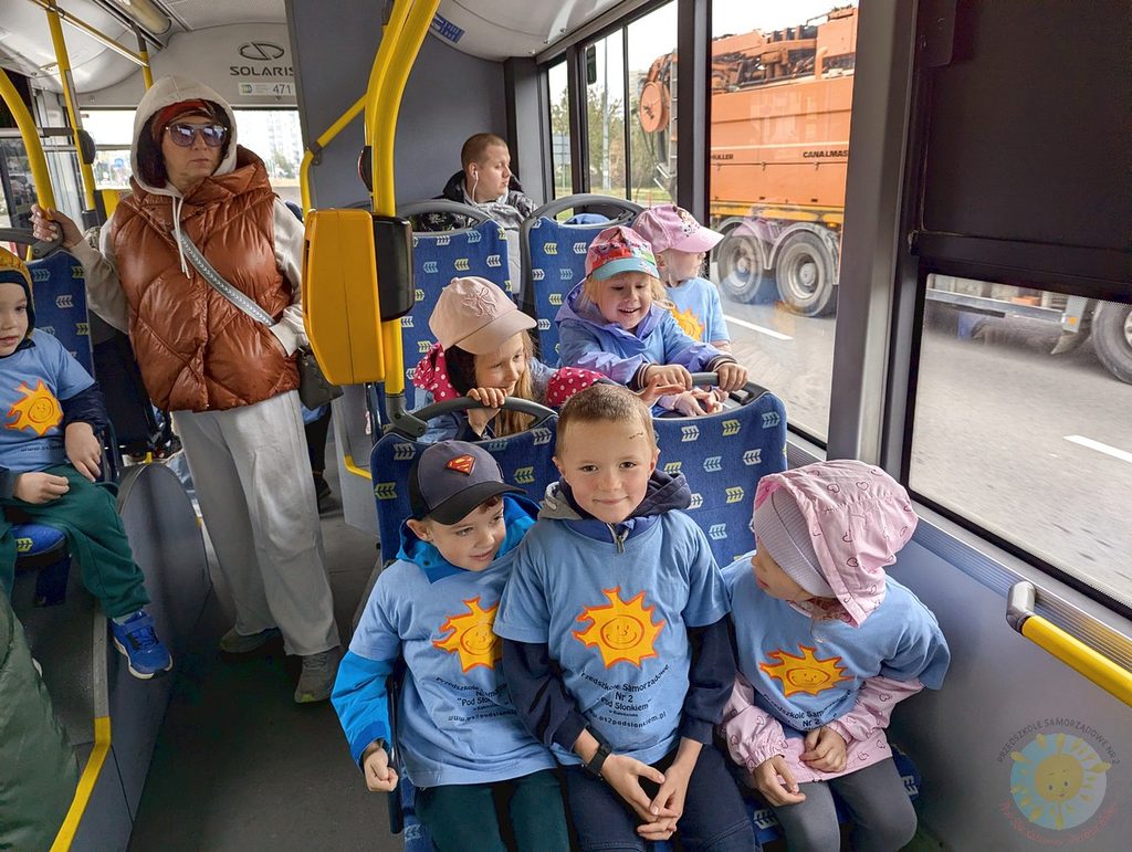 Dzieci w błękitnych koszulkach z logo przedszkola siedzą na miejscach w autobusie podczas wycieczki.