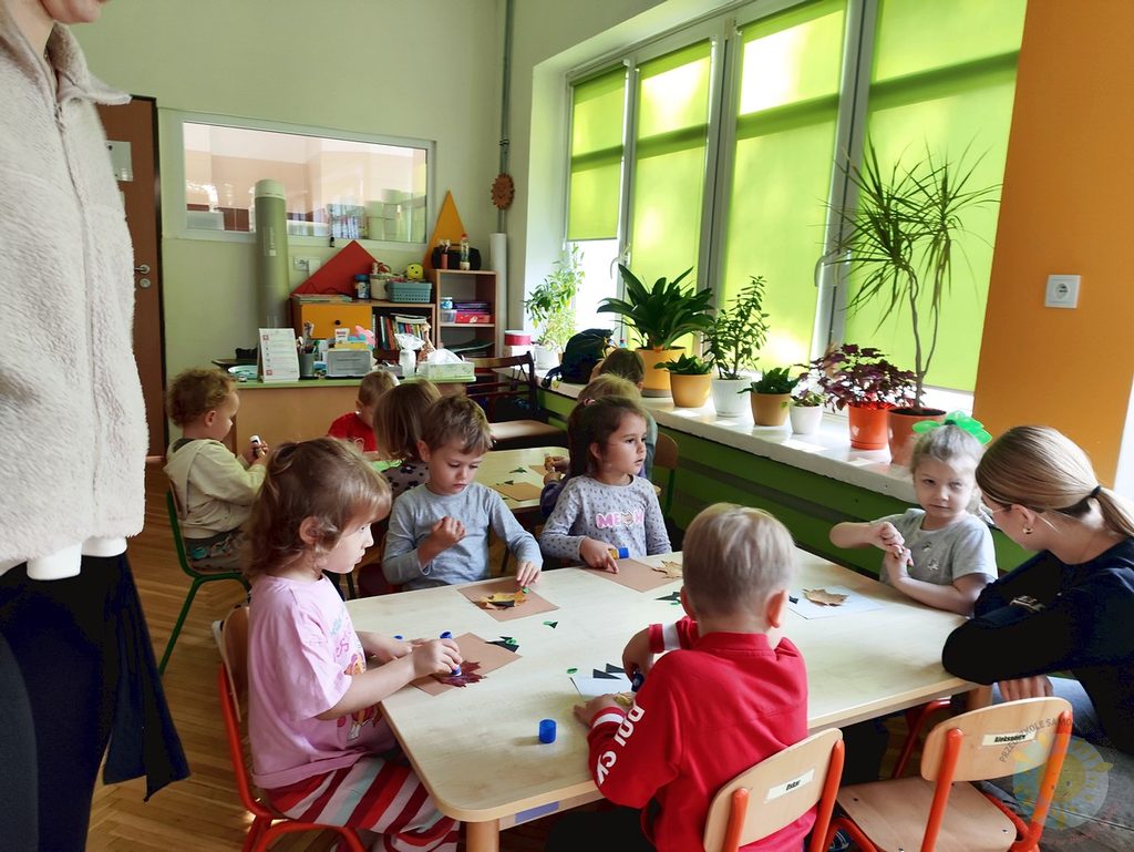 Dzieci siedzące przy stolikach w sali przedszkolnej podczas zajęć plastycznych z użyciem kolorowych liści.